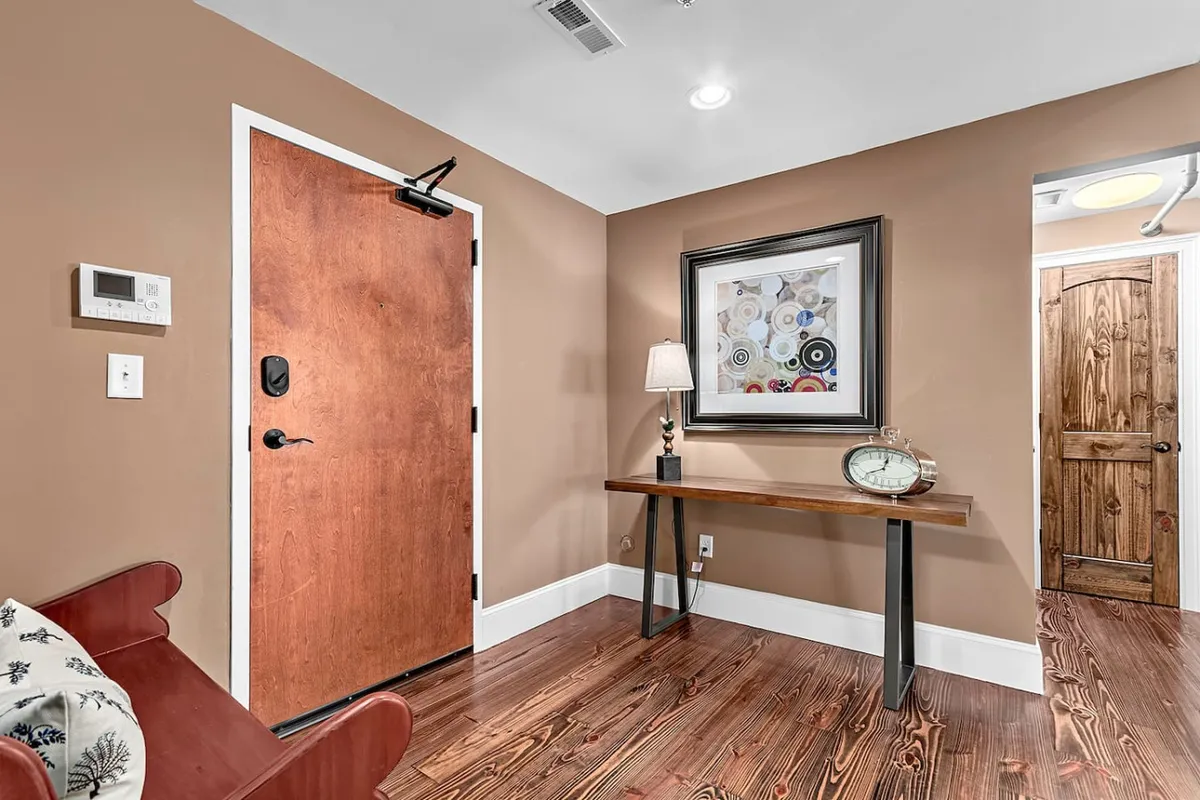 A stylish and secure lobby area featuring an entrance door, decorative artwork, a table lamp, console table, and wall clock. The ambiance is inviting, setting the tone for comfort and professionalism right from the building’s entrance.