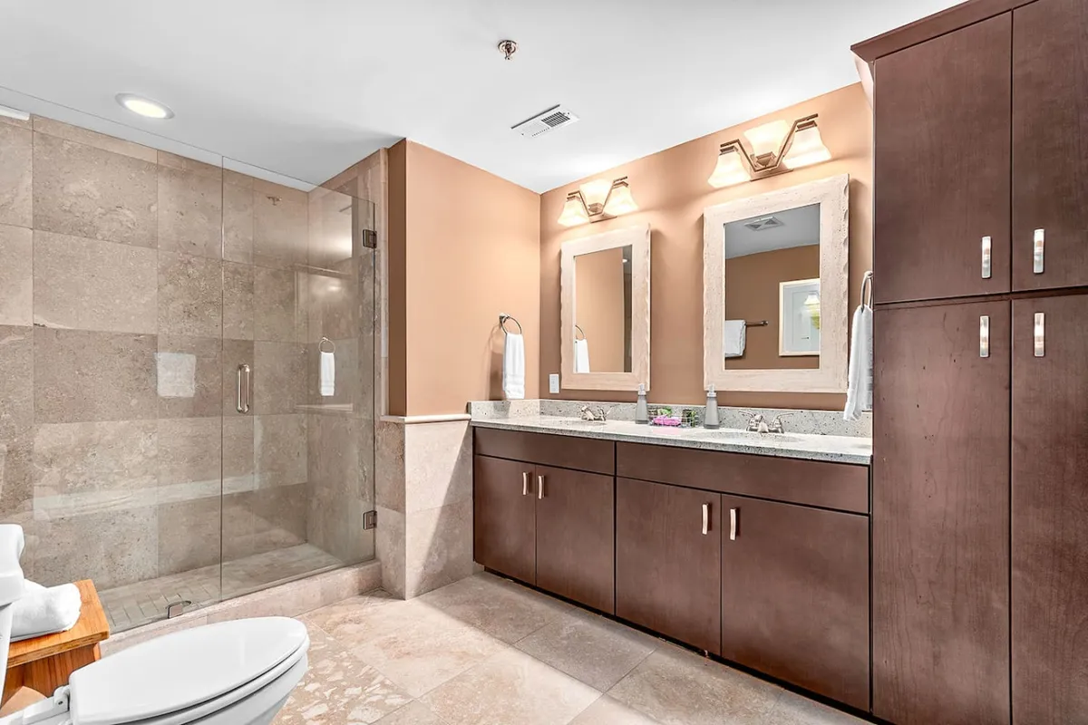 A spa-inspired bathroom featuring double vanities with expansive mirrors, a sleek glass shower enclosure, and granite countertops. The organized, serene space invites moments of relaxation and pampering.