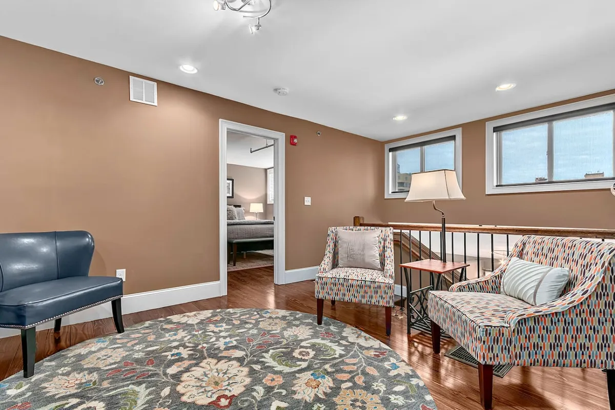 A comfortable living area with a mix of blue and patterned armchairs, a round area rug, and a side table with a lamp, suggesting a cozy spot for coffee, conversation, or relaxing before or after a meal.